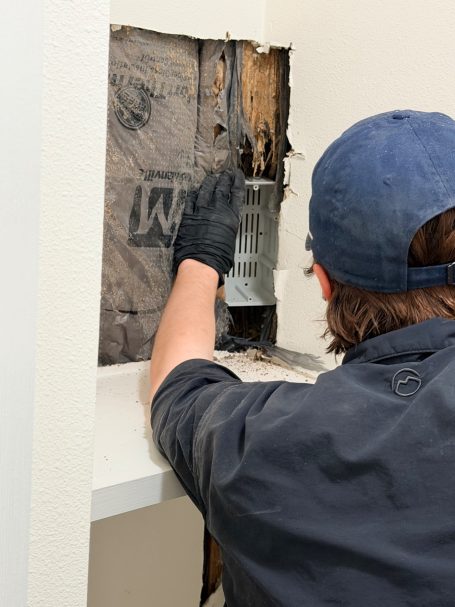 Technician installing an above-ground termite bait station inside an opened bathroom wall where Formosan termites were found.