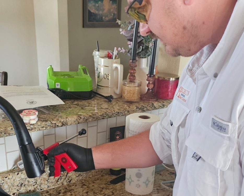 Pest control technician applying cockroach gel bait near a kitchen sink in a Daphne, AL home