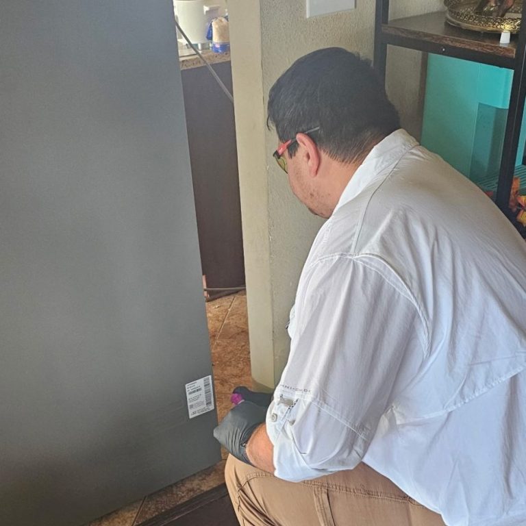 We Find Ants Where They Actually Live—Even Behind Appliances Hilbun Pest Control technician inspecting behind refrigerator for ant activity in residential kitchen in Baldwin County