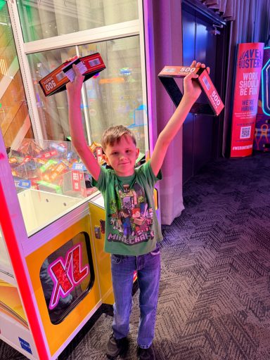 Noah Celebrates Big Win at Dave & Buster's Mobile Noah holding prize boxes after winning tickets from a claw machine at Dave & Buster's in Mobile, Alabama.
