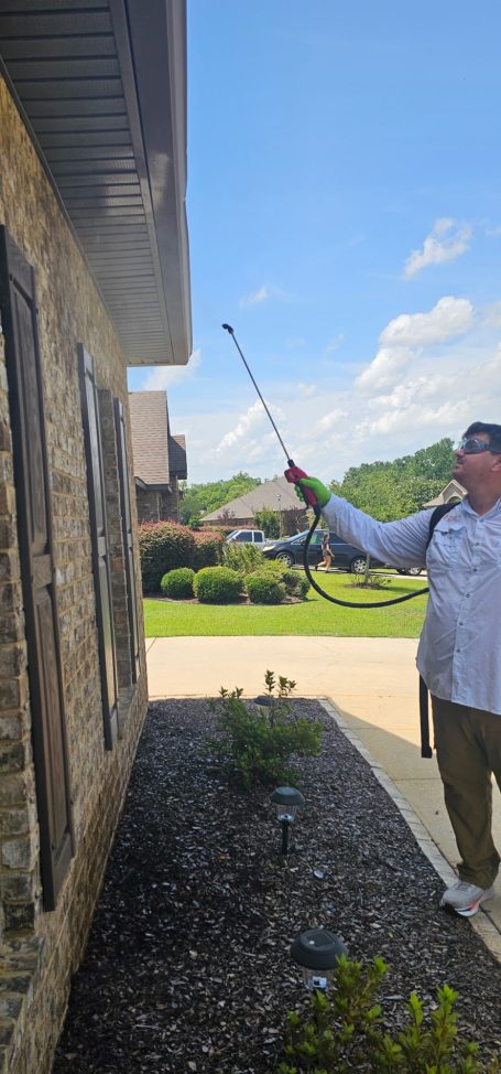 Hilbun Pest Control technician using a backpack sprayer to treat underneath the eaves of a home.