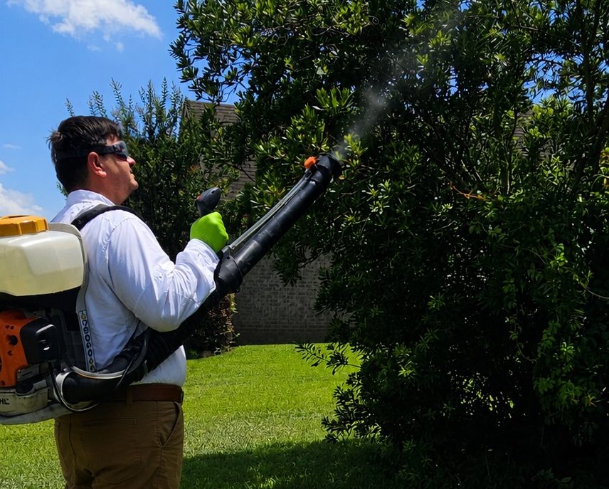Hilbun Pest Control technician treating shrubs with a backpack mist blower to reduce mosquitoes around a residential property.