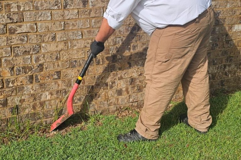 Pest control technician using a shovel to dig a termite treatment trench around a brick home slab in Daphne Alabama