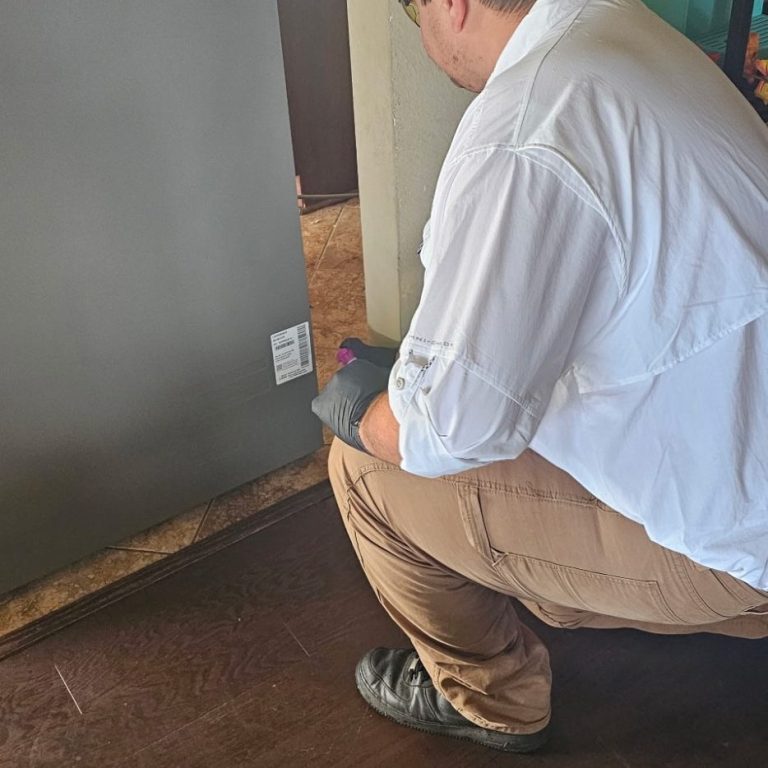 Pest control service in Daphne, Alabama kitchen behind refrigerator Technician performing pest control treatment behind refrigerator in Daphne, Alabama home